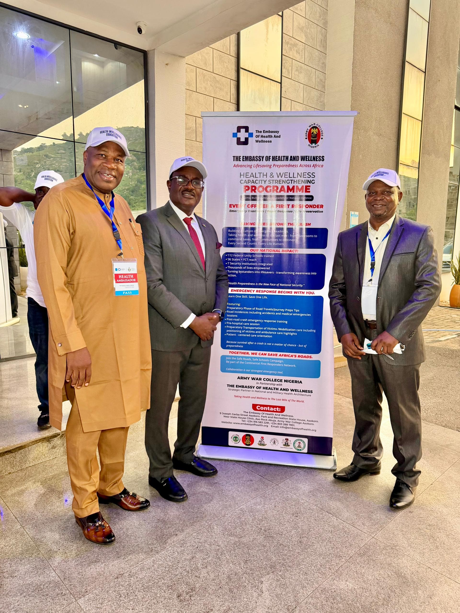 Three Health Ambassadors standing beside the Health & Wellness Capacity Strengthening Programme banner